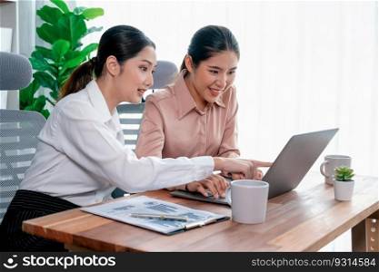 Two young office lady colleagues collaborating in modern office workspace, engaging in discussion and working together on laptop, showcasing their professionalism as modern office worker. Enthusiastic. Two young businesswoman work together in office workspace. Enthusiastic
