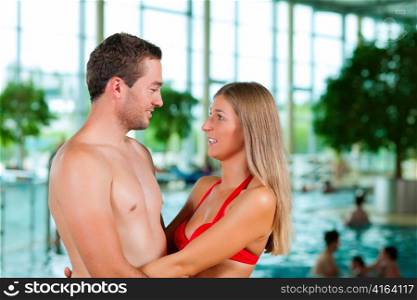 Two young people ? a couple - at a public swimming pool standing in front of the water
