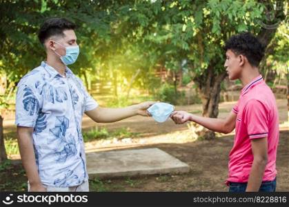 Two young people giving each other a mask, image of a young man giving a mask to another person, concept of a person offering a mask