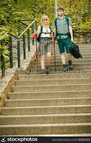 Two young people tourists hiking walking on stairs. Man and woman with trekking poles sticks.. Two people tourists hiking walking on stairs.