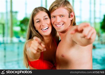 Two young people - woman and man - at a public swimming pool standing in front of the water