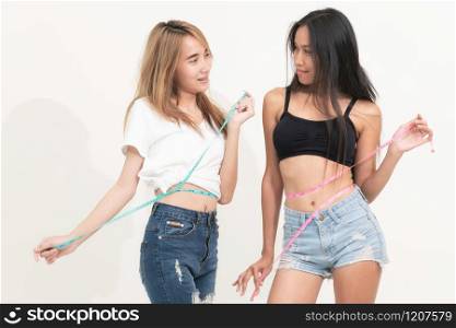 Two young slim woman measure their waist by measuring tape after diet against white backgrounds. Concept of weight loss success and slimming competitions.. Two slim woman measure waist with measuring tape.