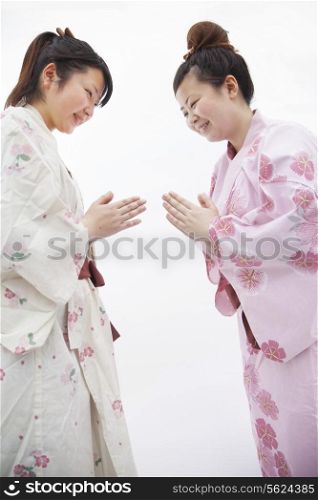 Two young smiling woman in Japanese kimonos bowing to each other, studio shot