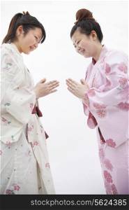 Two young smiling woman in Japanese kimonos bowing to each other, studio shot