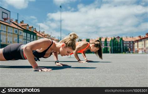 Two young sportswomen doing push-ups on a sports field. Sportswomen doing push-ups