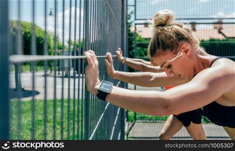 Two young sportswomen supported on the fence of a sports field. Two sportswomen supported on a fence