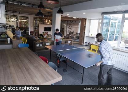 Two young start up business man playing ping pong tennis at modern creative office space people group have meeting and brainstorming in background