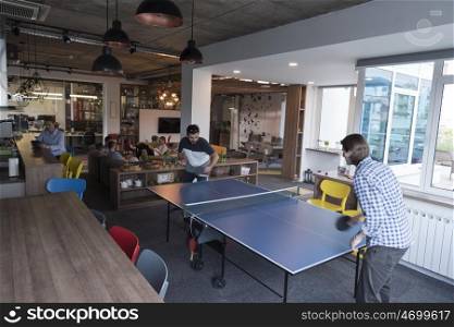 Two young start up business man playing ping pong tennis at modern creative office space people group have meeting and brainstorming in background