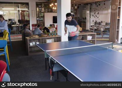 Two young start up business man playing ping pong tennis at modern creative office space people group have meeting and brainstorming in background