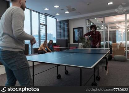 Two young start-up businessmen playing ping pong tennis at modern creative office space people group have meeting and brainstorming in background. High-quality photo. Two young start up business man playing ping pong tennis at modern creative office space people group have meeting and brainstorming in background