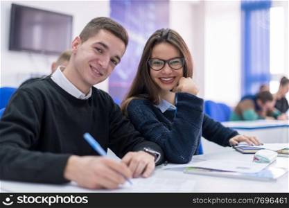 Two young students man and woman with others working on a project in a classroom writing notes  and discussing