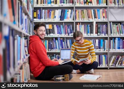 two young students sit in the school library and use a laptop to take notes