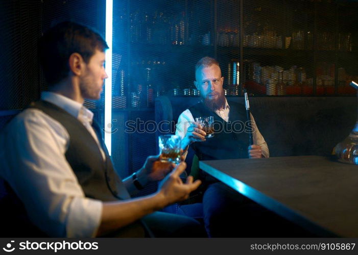 Two young stylish man relax and smoking hookah in bar. Business friends smoke from shisha pipe and drinking in the restaurant. Two young stylish man relax and smoking hookah in bar