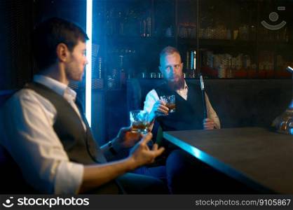 Two young stylish man relax and smoking hookah in bar. Business friends smoke from shisha pipe and drinking in the restaurant. Two young stylish man relax and smoking hookah in bar