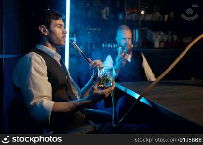Two young stylish man relax and smoking hookah in bar. Business friends smoke from shisha pipe and drinking in restaurant. Two young stylish man relax and smoking hookah in bar