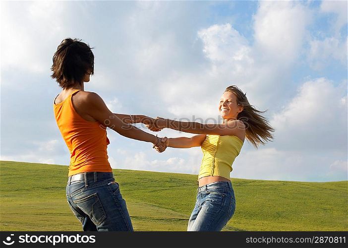 Two young swinging each other around in mountain field, side view