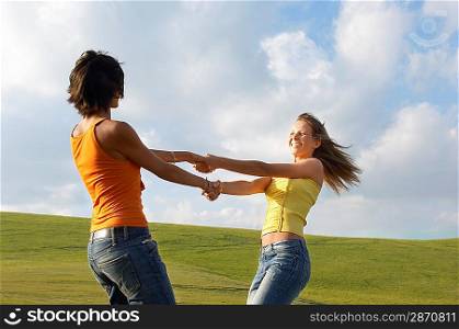Two young swinging each other around in mountain field, side view