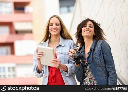 Two young tourist women looking maps with digital tablet outdoors. Travelers concept.