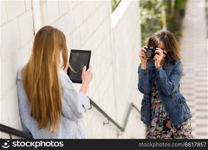 Two young tourist women taking photographs with digital tablet and analogic reflex camera. Travelers concept.