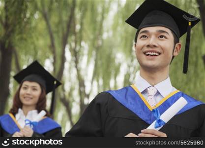 Two Young University Graduates Holding Diplomas, Man in Front
