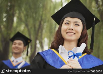 Two Young University Graduates Holding Diplomas, Woman in Front