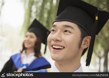 Two Young University Graduates Looking Away, Man in Front