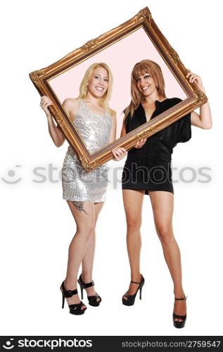Two young woman, blond and brunette, in short evening dress and highheels, holding a picture frame up and looking trough, for white background.
