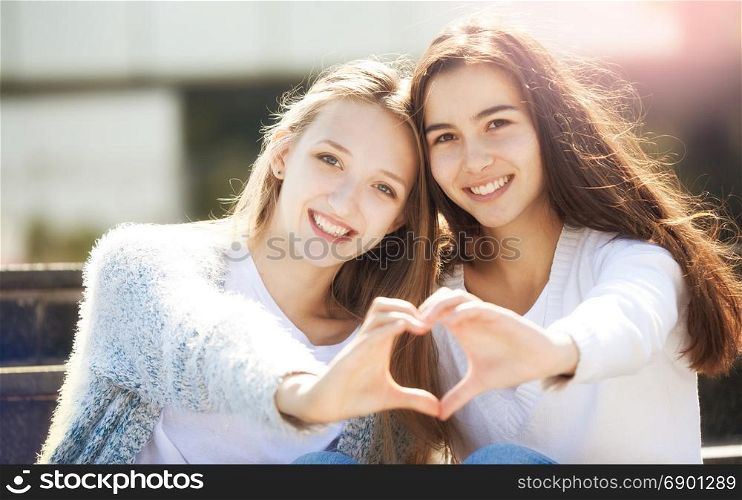 Two Young Woman Holding Hands in the Shape of a Heart and Smiling, Looking at the Camera