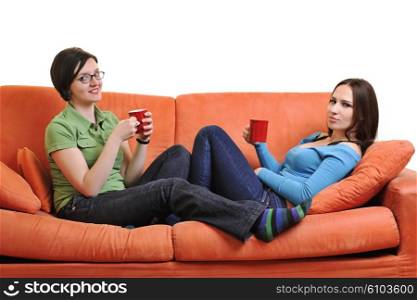 two young woman isolated on white with cup off coffee talking and chating isolated on whtie on orange sofa