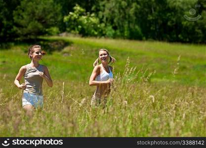 Two young woman jogging in a meadow on sunny day