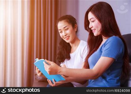 two young woman reading a book on sofa in living room at home