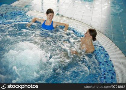 Two young woman rest in bubbling hot tub at swimming pool. Female sportswoman enjoying hydrotherapy treatment taking bubble bath to relax after training class. Two young woman rest in bubbling hot tub at swimming pool