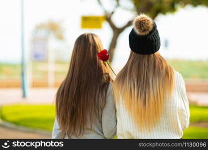 Two young woman&rsquo;s turning its back on the camera and a rose in the middle.. Young couple turning its back on the camera
