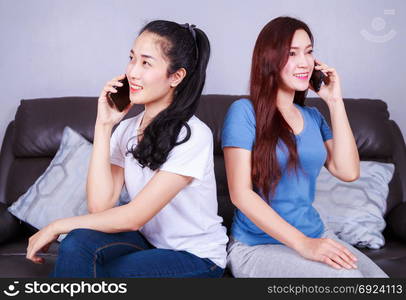 two young woman talking on mobile phone on sofa in living room at home