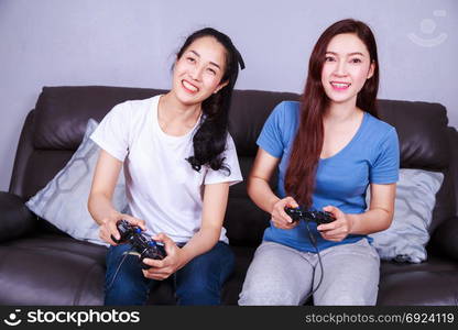 two young woman using joystick controller playing video game on sofa in living room at home