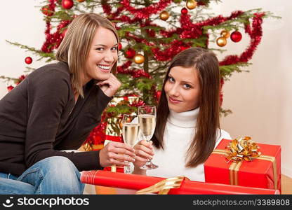 Two young woman with champagne and Christmas tree and present