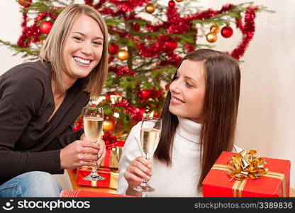 Two young woman with champagne and Christmas tree and present