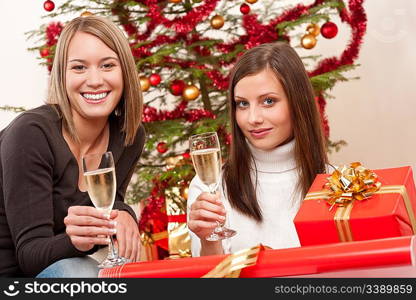 Two young woman with champagne and Christmas tree and present