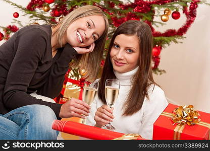 Two young woman with champagne and Christmas tree and present