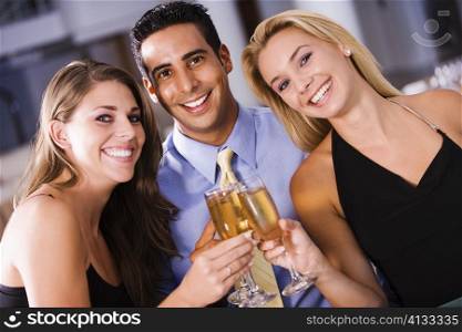 Two young women and a mid adult man toasting with champagne flutes