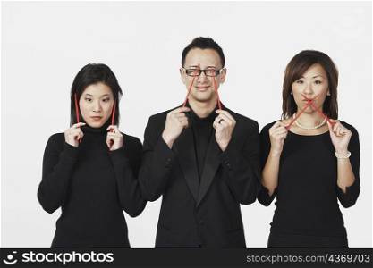 Two young women and a young man gesturing speak no evil, hear no evil, see no evil with chopsticks