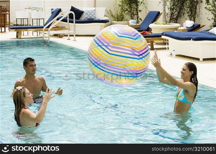 Two young women and a young man playing with a beach ball in a swimming pool