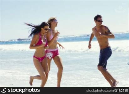 Two young women and a young man running on the beach