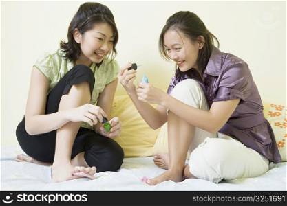 Two young women applying nail polish on their toenails