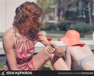 Two young women are relaxing on the grass outside in an urban area on a sunny day