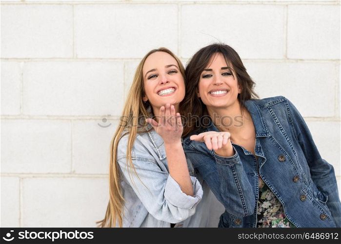 Two young women blowing a kiss on urban wall.. Two beautiful girls blowing a kiss on urban wall outdoors. Young women wearing casual clothes.
