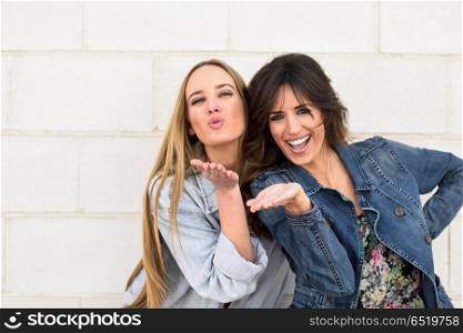 Two young women blowing a kiss on urban wall.. Two young women blowing a kiss on urban wall outdoors.