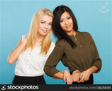 Two young women caucasian and mixed race in trendy clothes posing studio portrait on blue