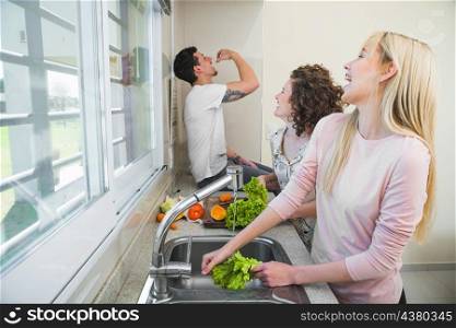 two young women cleaning lettuce vegetable laughing while looking man eating carrot