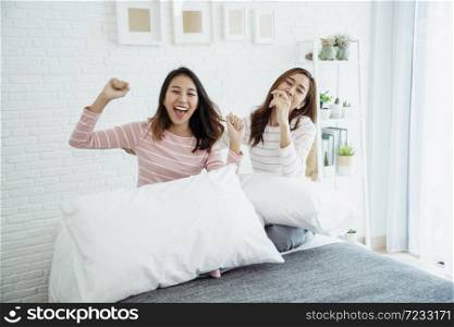 Two young women dance laughing together happy friendship smile with happiness in bedroom wear casual dress on bed. Happy girl friends dance to celebrate good news together at home. Woman joyful laugh